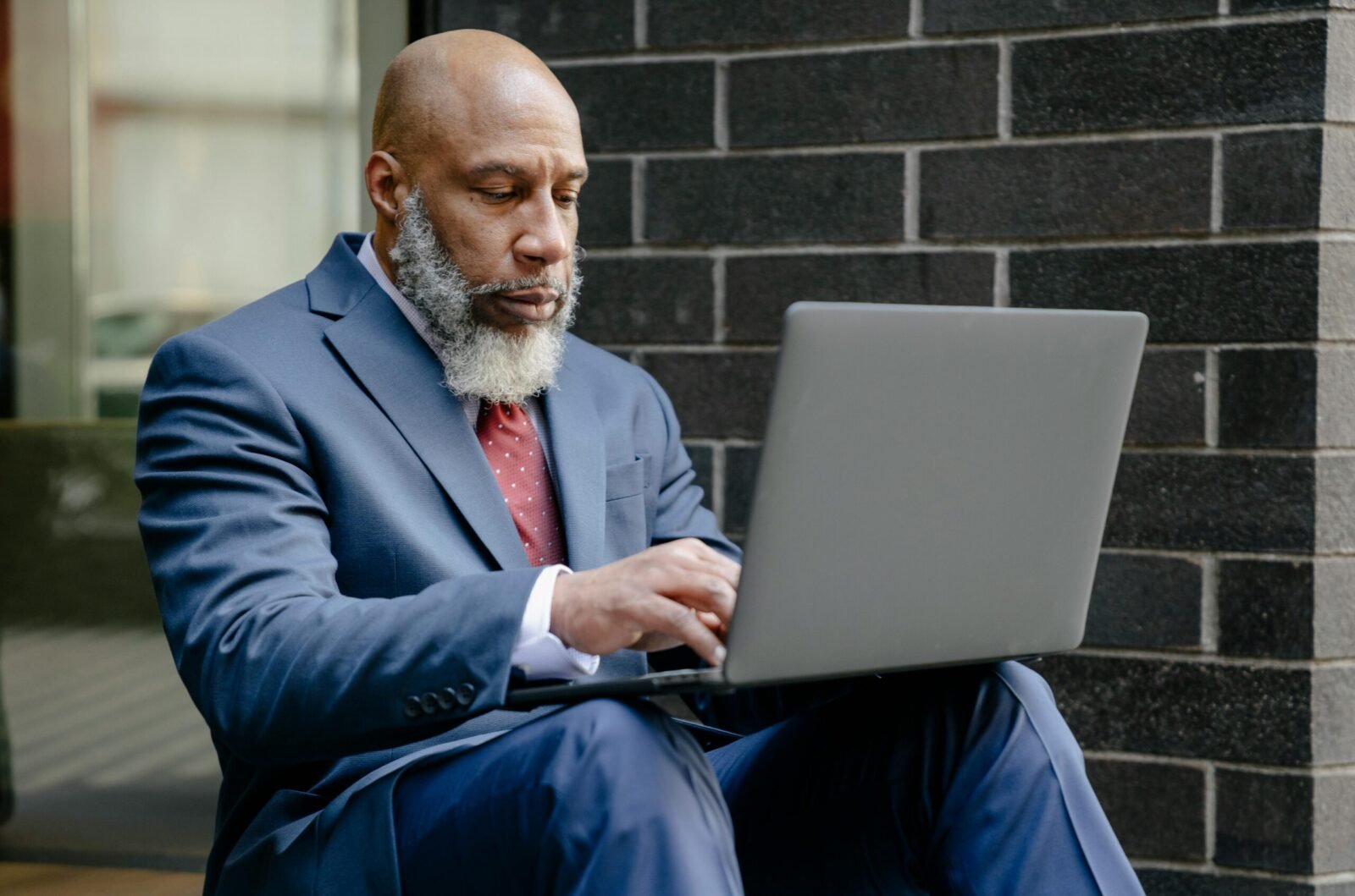 Mature African American businessman using a laptop while sitting outdoors, dressed in a suit.